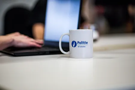 Koffiemok van Lokale Politie Schoten op een tafel voor een laptop