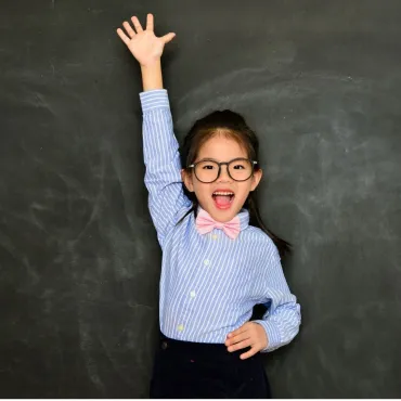 vrolijk meisje met bril steekt hand op voor schoolbord